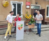 Przemowa pani Sołtys, podczas kiedy radny Jan Lazurko poprawia mikrofon, Wójt gminy stojący z boku